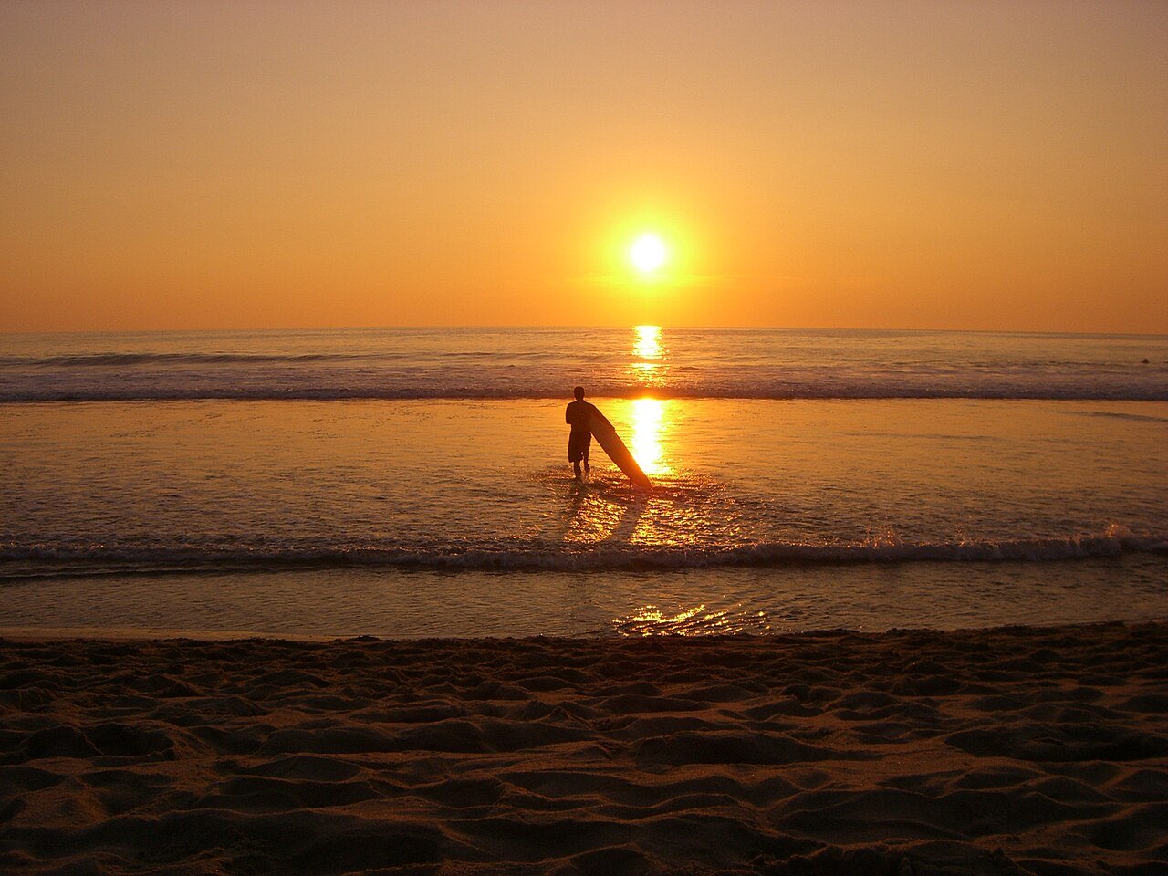 A surfer carrying a board on the beach at sunset at Zicatela in Puerto Escondido