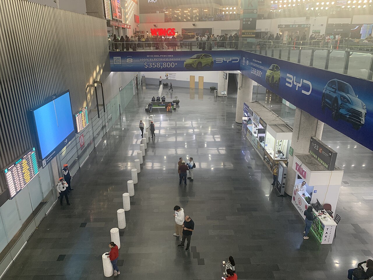 Arrivals hall at Terminal 2 of Mexico City airport seen from above, with a ticket counter on the right for authorized taxis