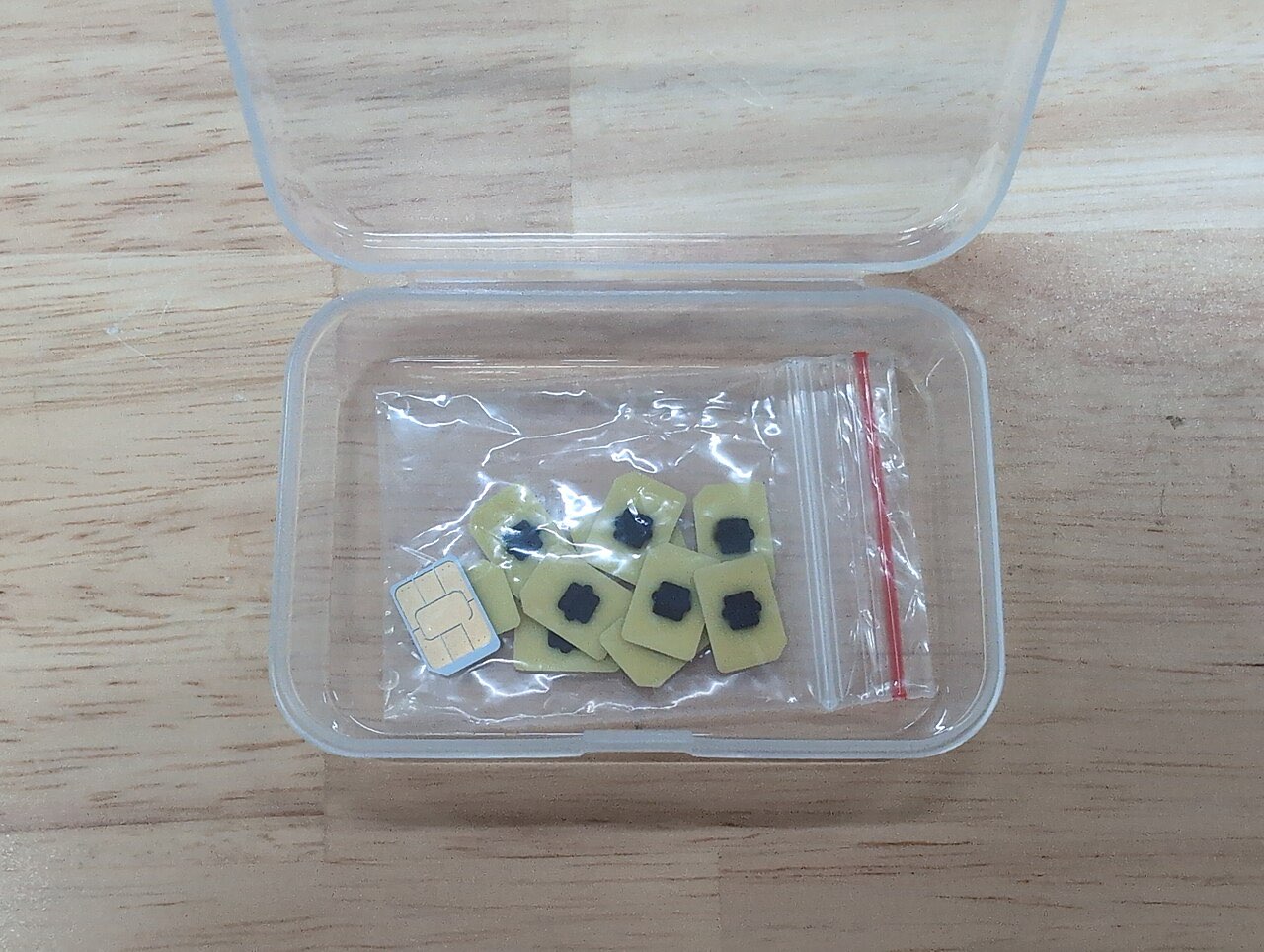 A small clear box holding loose eSIM chip modules and one nano SIM card on a wooden table