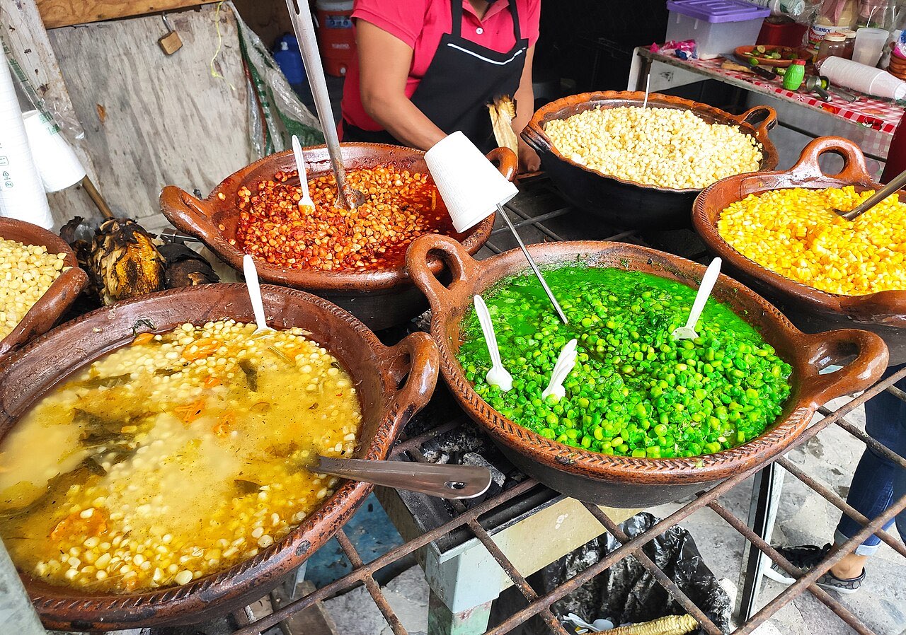 Clay cazuelas of esquites in different colors and chile preparations at a street stall